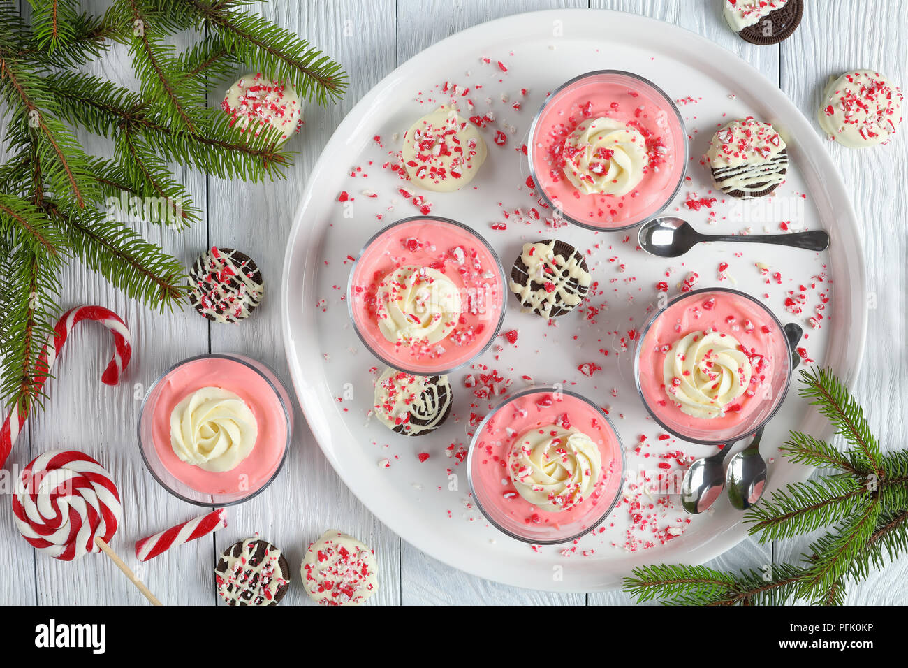Cheesecake sans cuisson garnie de mousse de crème fouettée, saupoudrée de cannes de bonbon broyées dans du verre tasses sur plateau avec des branches de sapin, bonbons et biscuits à Banque D'Images