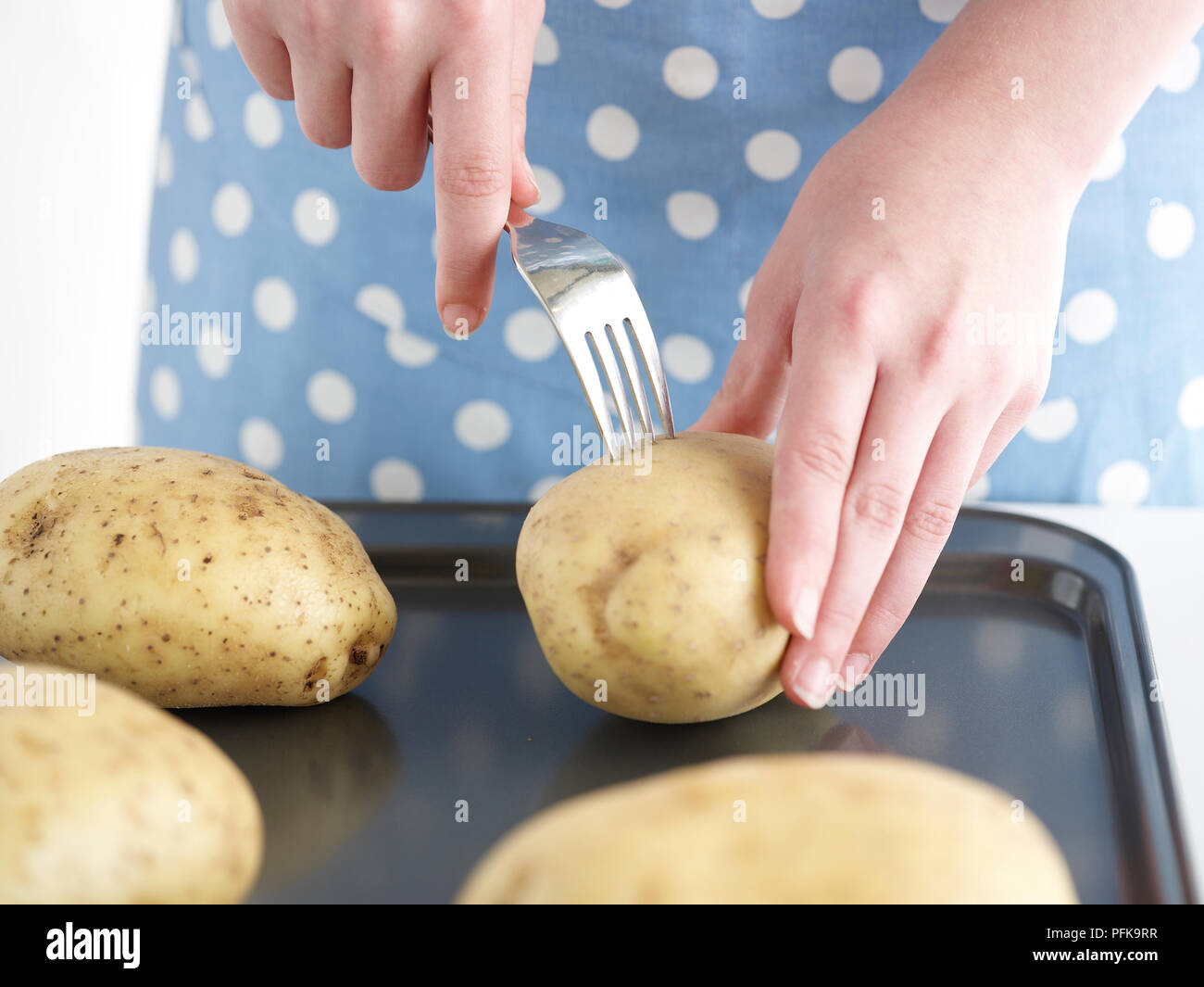 Young woman's hands, piquer avec une fourchette de pommes de terre au four, sur la plaque de cuisson Banque D'Images