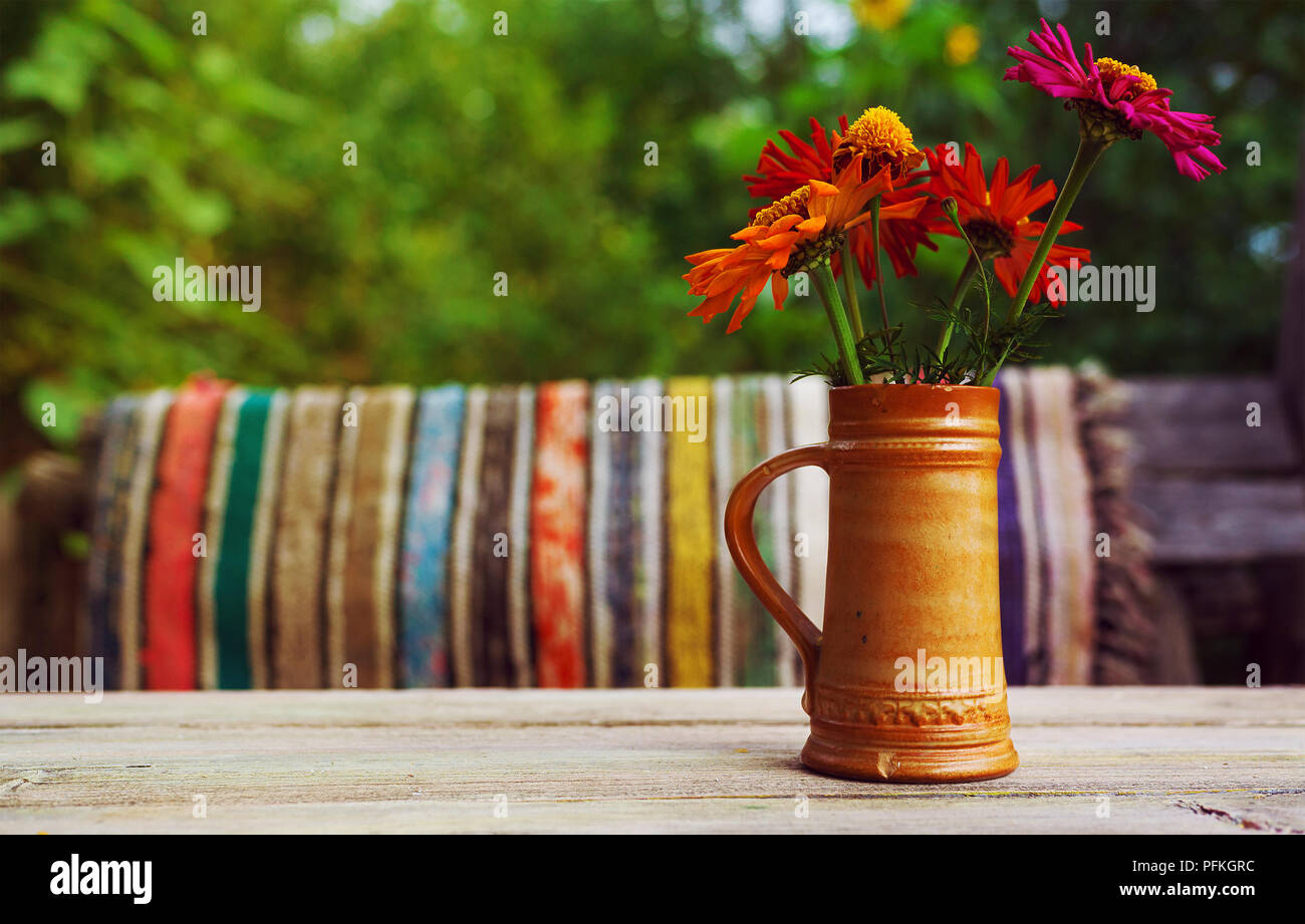 Des fleurs colorées dans la vieille tasse en céramique sur la vieille table en bois, tapis colorés en arrière-plan. Banque D'Images
