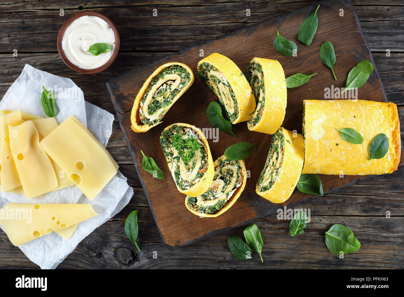 Roulade oeufs délicieux avec un remplissage de mélange d'épinards, la feta et les carottes coupées en tranches sur les planches à découper en bois avec la sauce et le fromage sur la table, Banque D'Images