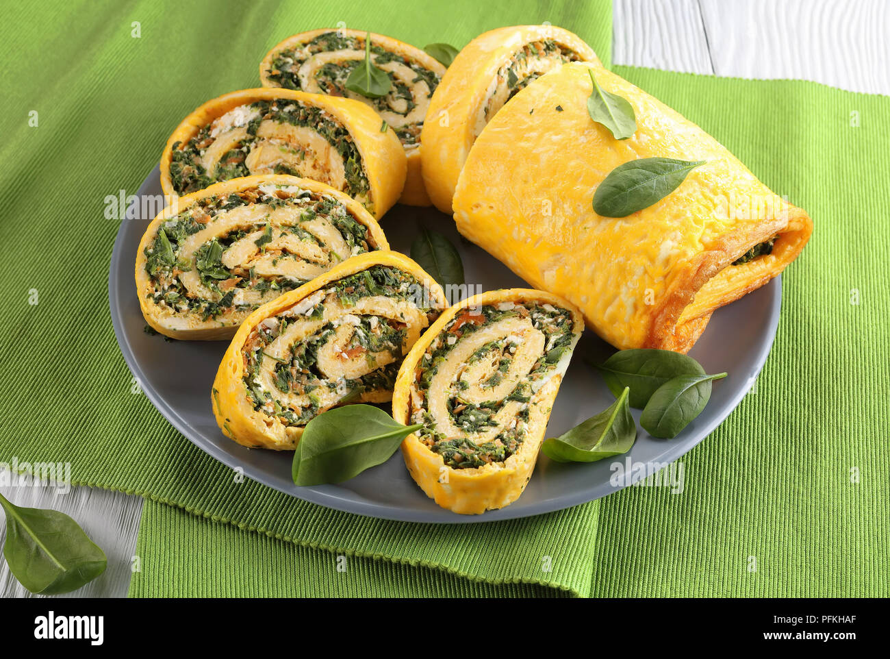 Roulade oeufs délicieux avec un remplissage de mélange d'épinards, la feta et les carottes coupées en tranches sur la plaque grise sur le textile vert mat sur table en bois, vie Banque D'Images