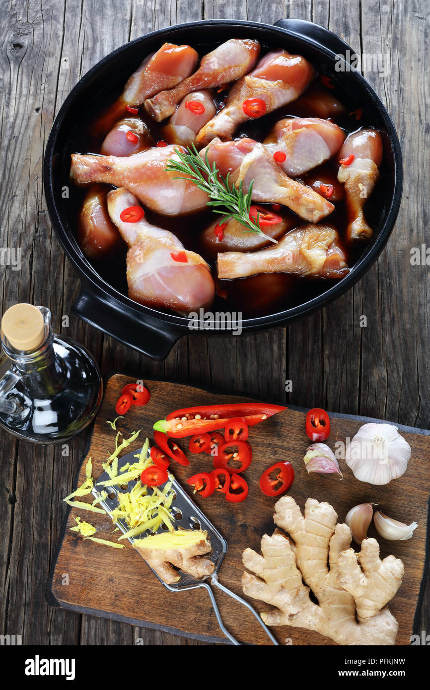 Pilons de poulet cru mariné à la sauce teriyaki épicé fait maison en noir plat. Ingrédients sur planche à découper en bois sur la table en bois, vue verticale Banque D'Images