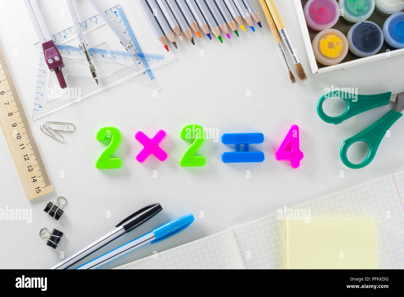 L'équation mathématique '2*2 =4' à partir de numéros en plastique de différentes couleurs sur un fond blanc avec des articles scolaires. Banque D'Images