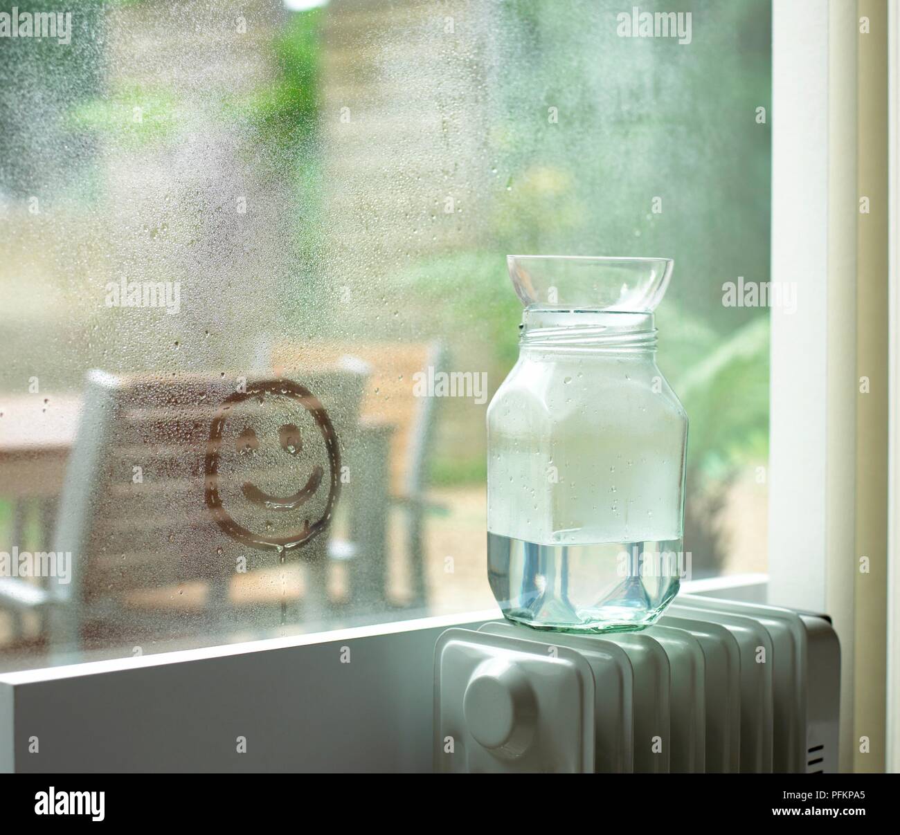 Pot d'eau et bol en verre sur le dessus du radiateur et smiley dessiné dans  la condensation sur la fenêtre Photo Stock - Alamy