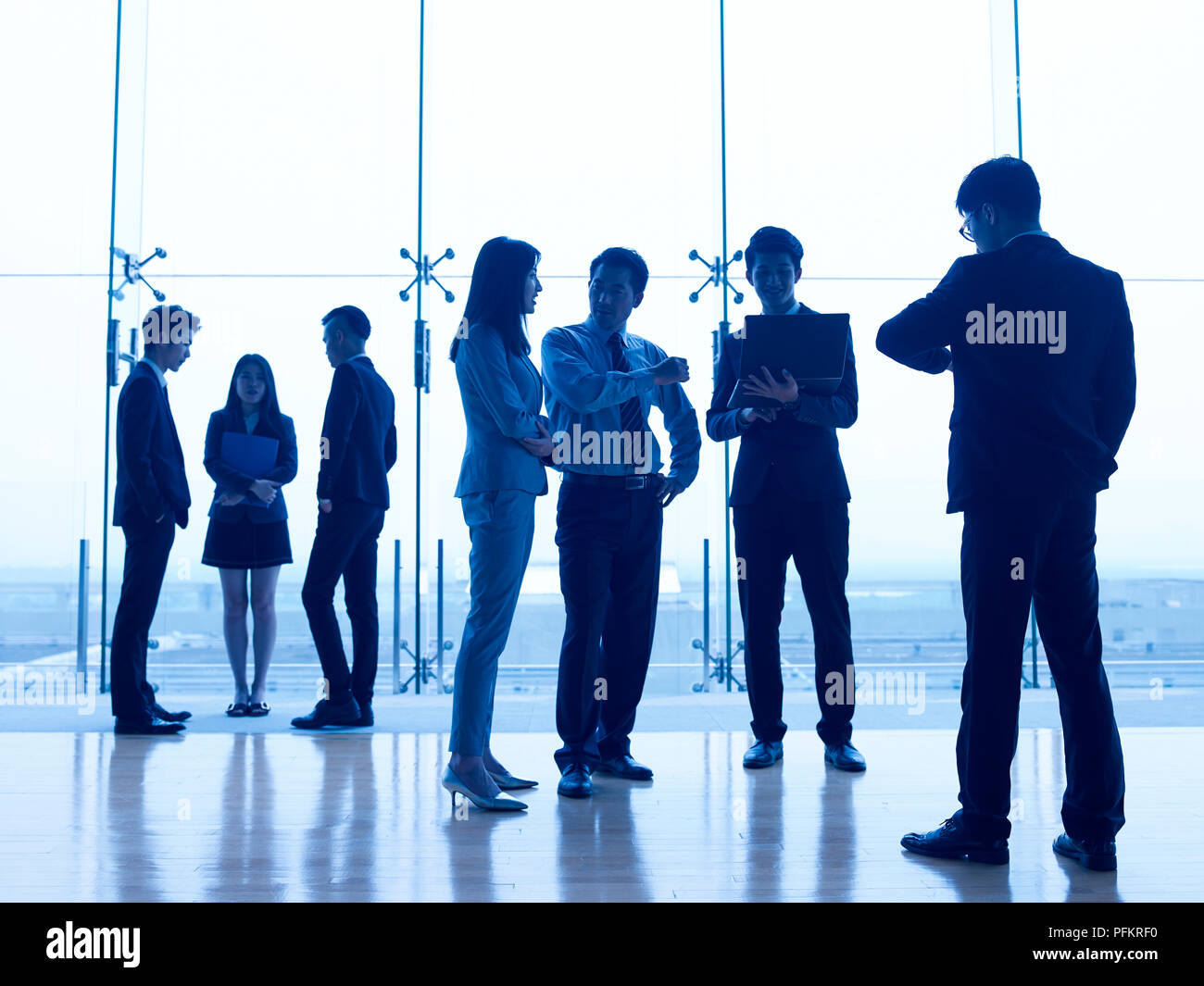 Silhouettes d'asian people standing parler affaires dans un bureau moderne. Banque D'Images