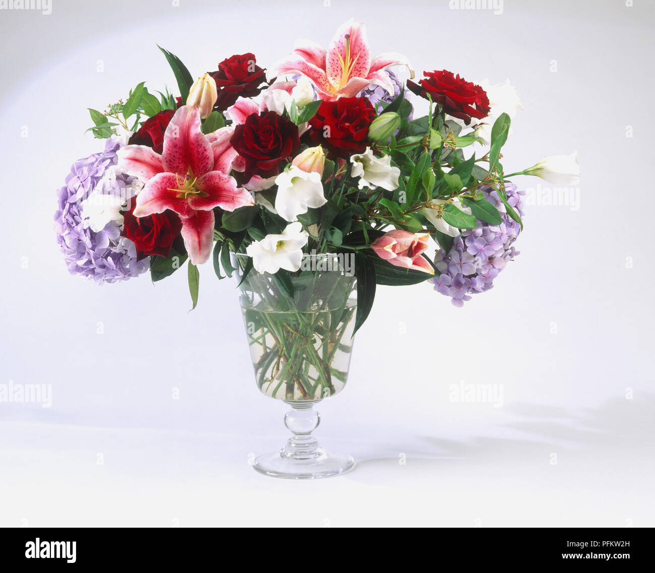 Un vase en verre contenant un gros bouquet de fleurs, notamment des roses, hortensias et nénuphars Banque D'Images