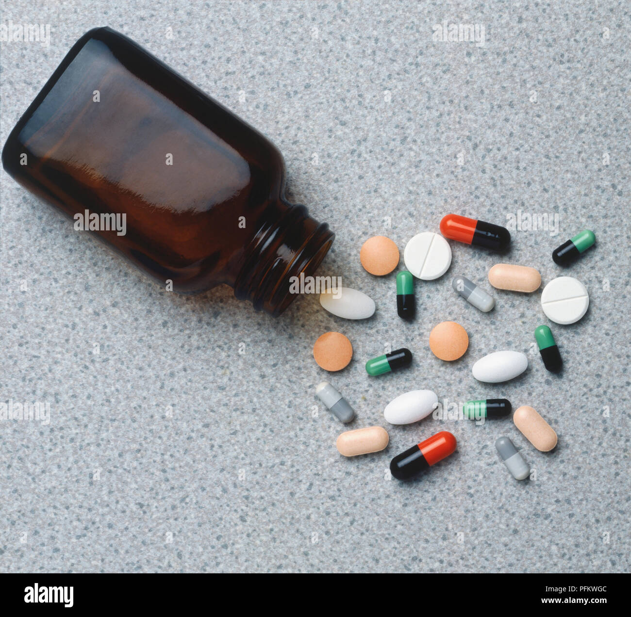 Sélection de pilules colorées disséminés en face d'un flacon en verre brun couché horizontalement sur le côté, Close up. Banque D'Images