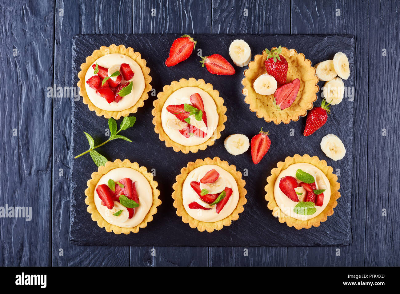 Tartelettes aux fraises, des tranches de banane chargé avec de la crème pâtissière - diplomat sur une plaque en ardoise noire, vue de dessus, close-up Banque D'Images
