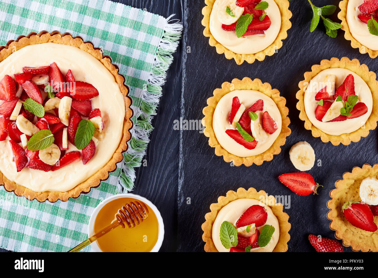 Tartelettes aux fraises, des tranches de banane chargé avec crème pâtissière sur une plaque en ardoise noire. tart dans un moule sur le tapis textiles Vue de dessus, fermer Banque D'Images
