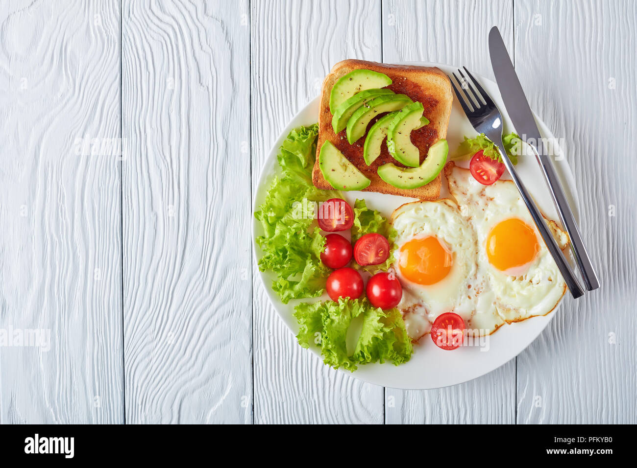 Petit-déjeuner australien sain - d'œufs au plat, une salade fraîche, des toasts avec de la levure et propagation de tranches d'avocat sur une plaque blanche sur une table en bois, vue du dessus Banque D'Images