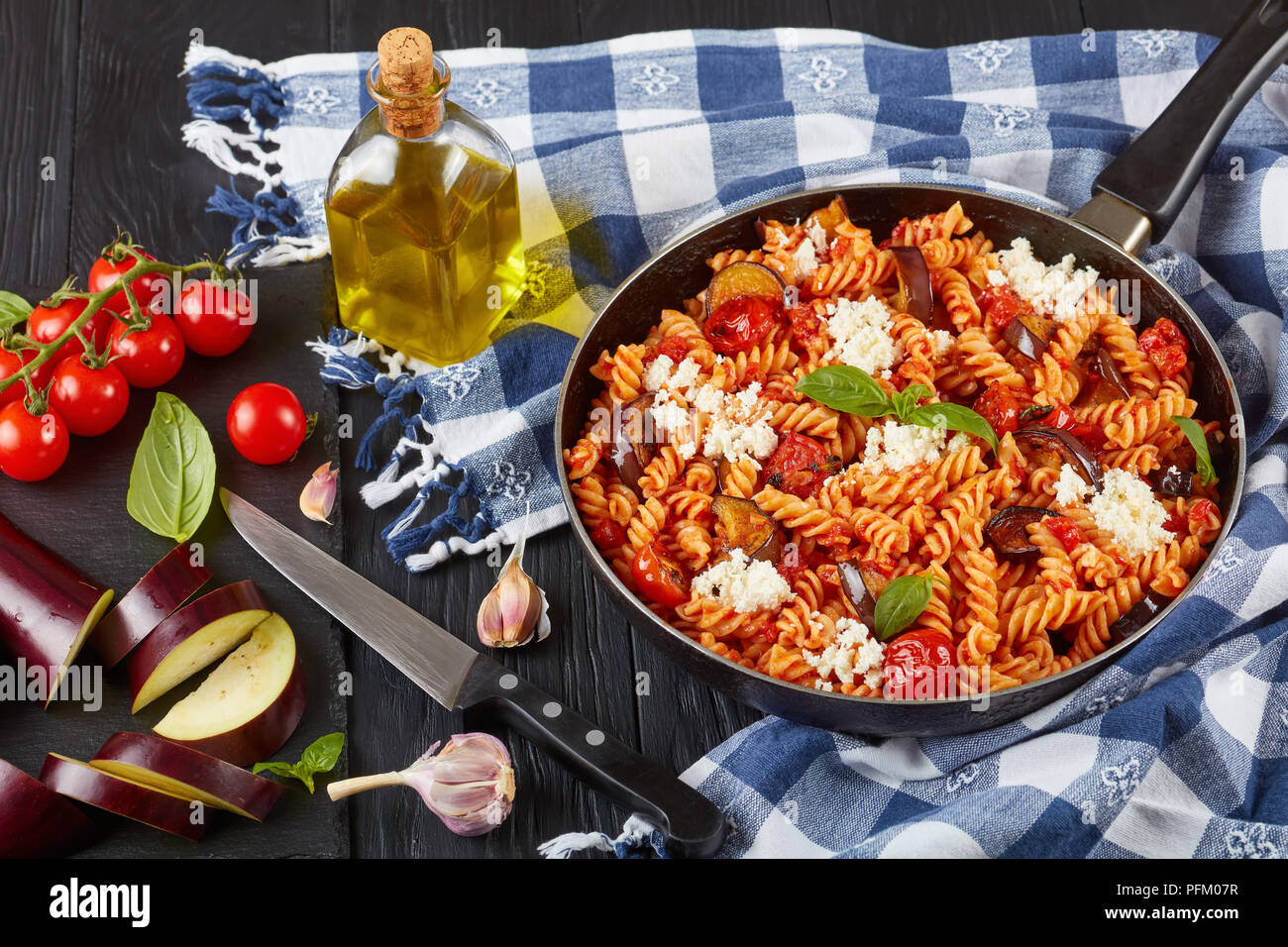 Les pâtes italiennes Les végétariens les fusilli alla Norma avec des aubergines, tomates, basilic, fromage ricotta et sauce marinara dans une poêle avec des ingrédients au bac Banque D'Images