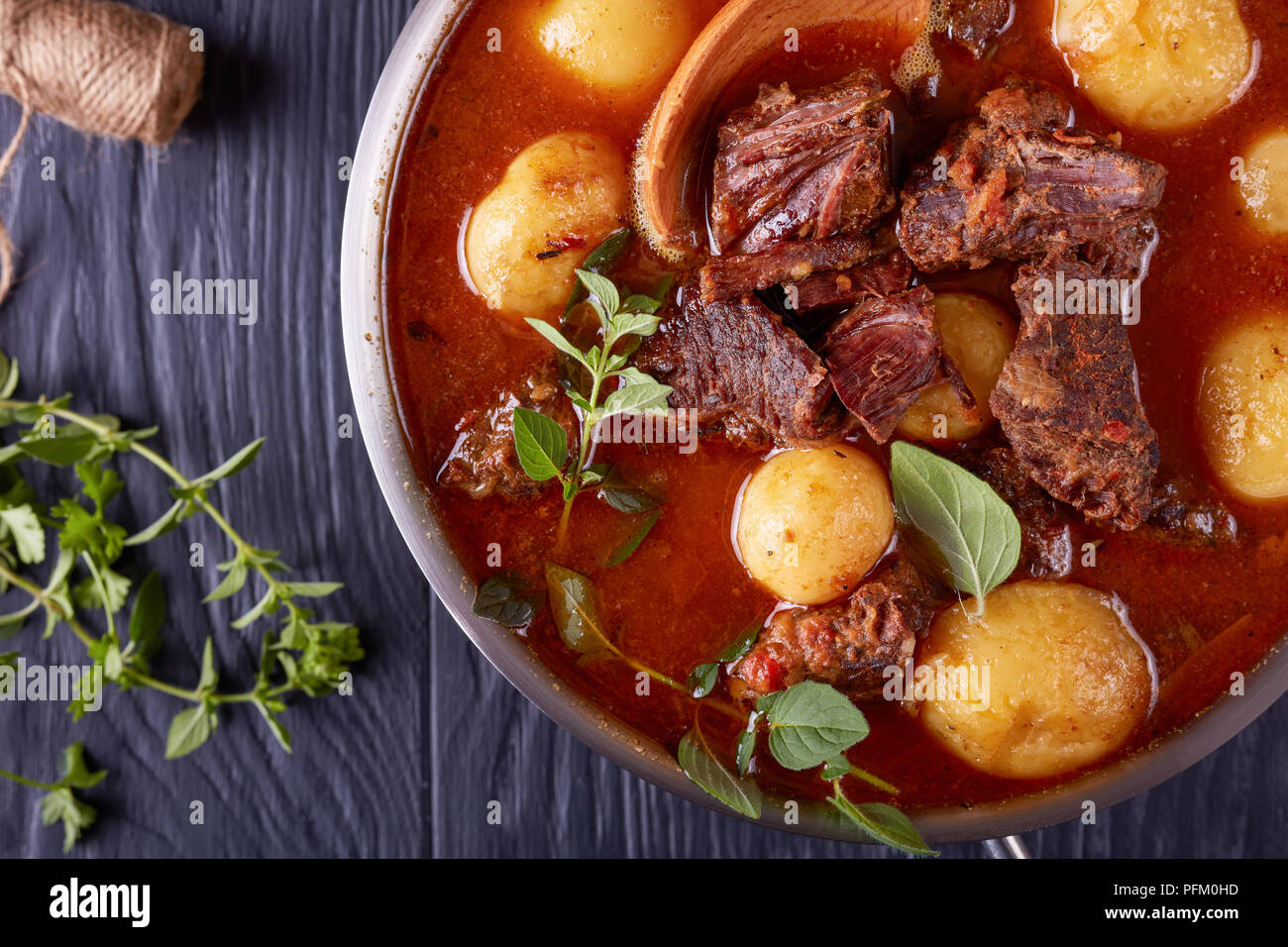 Ragoût de boeuf avec des cubes de viande tendre, ensemble de nouvelles pommes de terre, carottes et herbes dans un chaudron sur une table en bois noir avec bouquet d'herbes aromatiques, voir f Banque D'Images