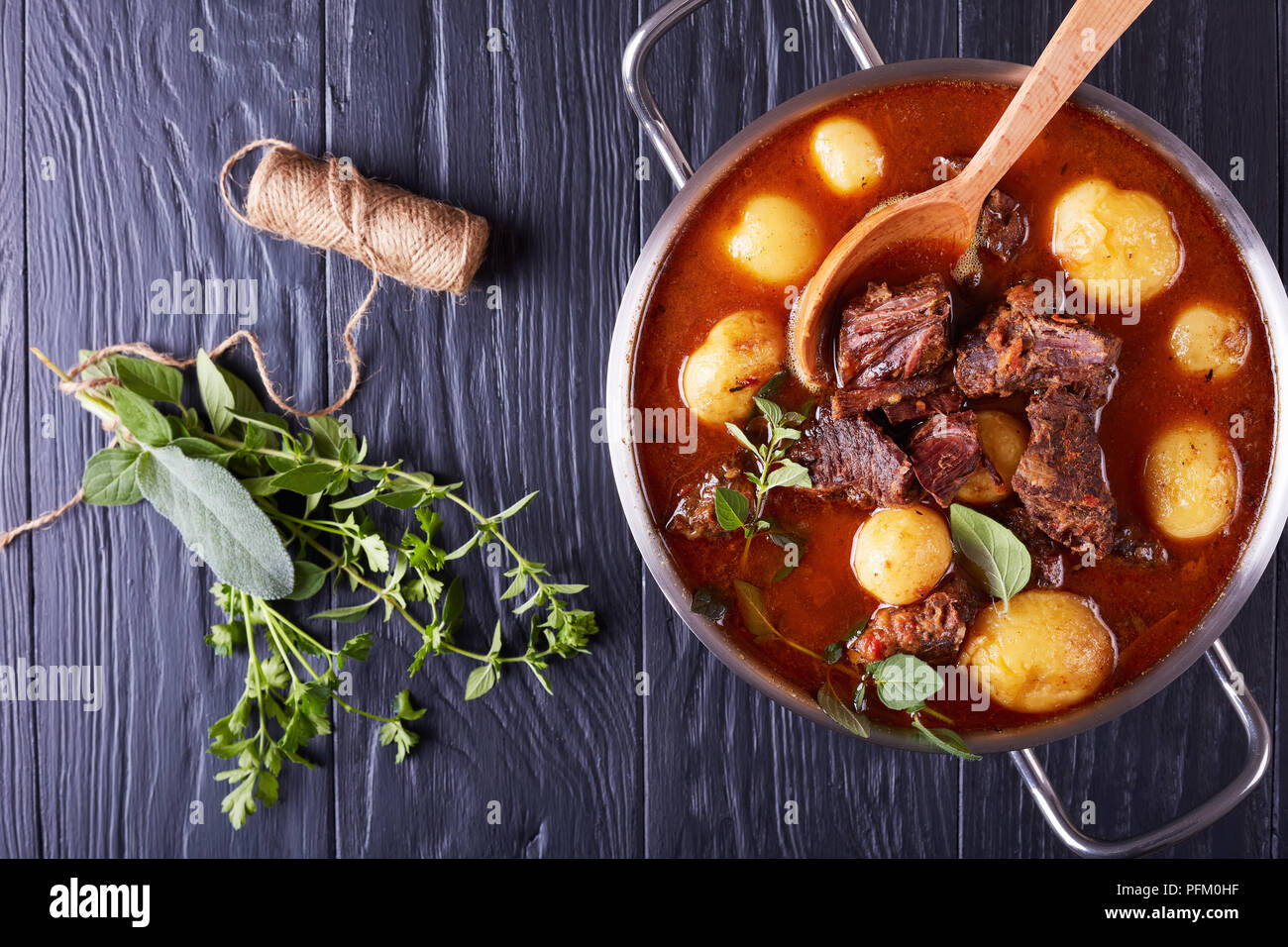 Ragoût de boeuf avec des cubes de viande tendre, ensemble de nouvelles pommes de terre, carottes et herbes dans un chaudron sur une table en bois noir avec bouquet d'herbes aromatiques, voir f Banque D'Images