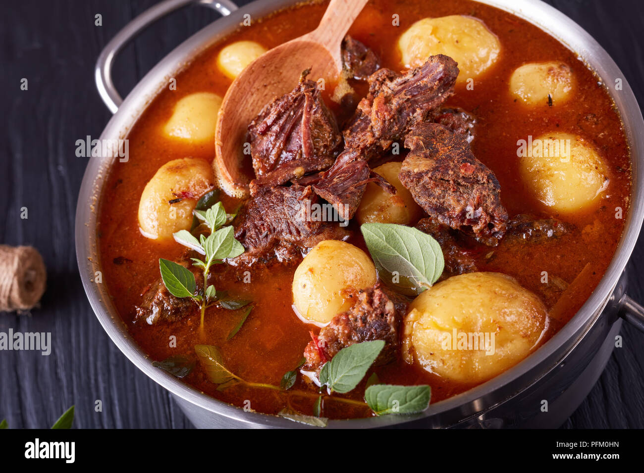 Ragoût de boeuf chaud avec de tendres cubes de viande, tout nouveau les pommes de terre, les carottes et les herbes dans un chaudron sur une table en bois noir avec bouquet d'herbes aromatiques, vi Banque D'Images