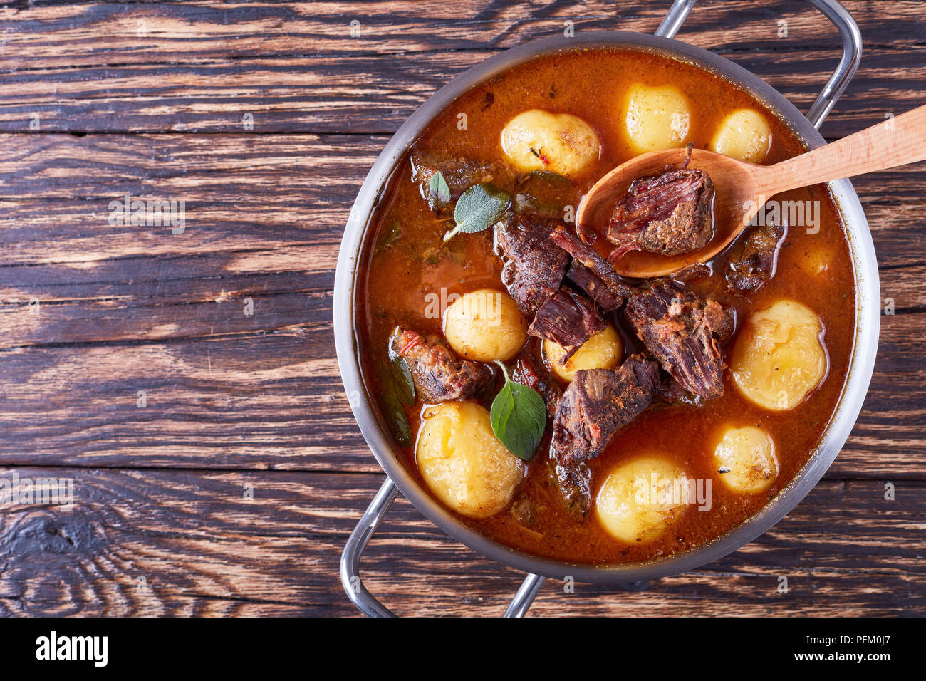 Ragoût de boeuf chaud avec de tendres cubes de viande, tout nouveau les pommes de terre, les carottes et les herbes dans une casserole de métal sur la vieille table en bois rustique, une cuisine irlandaise, horizon Banque D'Images