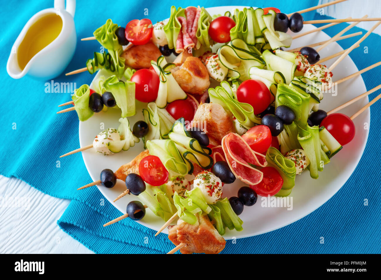 La viande de poulet shish kebab brochettes avec des rubans de courgettes, tomates, mozzarella tranches de salami, boules, olives noires sur une plaque blanche, vue horizontale à partir de Banque D'Images