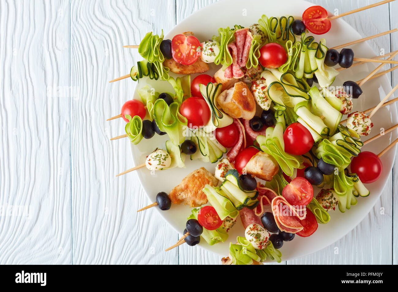 L'antipasto grillé brochettes de viande de poulet, courgettes, tomates crues rubans, boules de mozzarella chevronné, tranches de salami, olives noires sur une plaque blanche o Banque D'Images