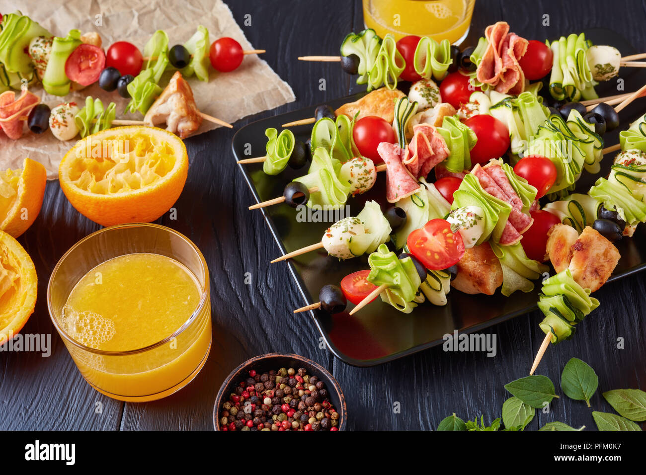 L'antipasto brochettes avec la viande de poulet, courgettes, tomates, mozzarella tranches de salami, boules, des olives sur une plaque noire sur une table en bois avec du jus d'orange Banque D'Images