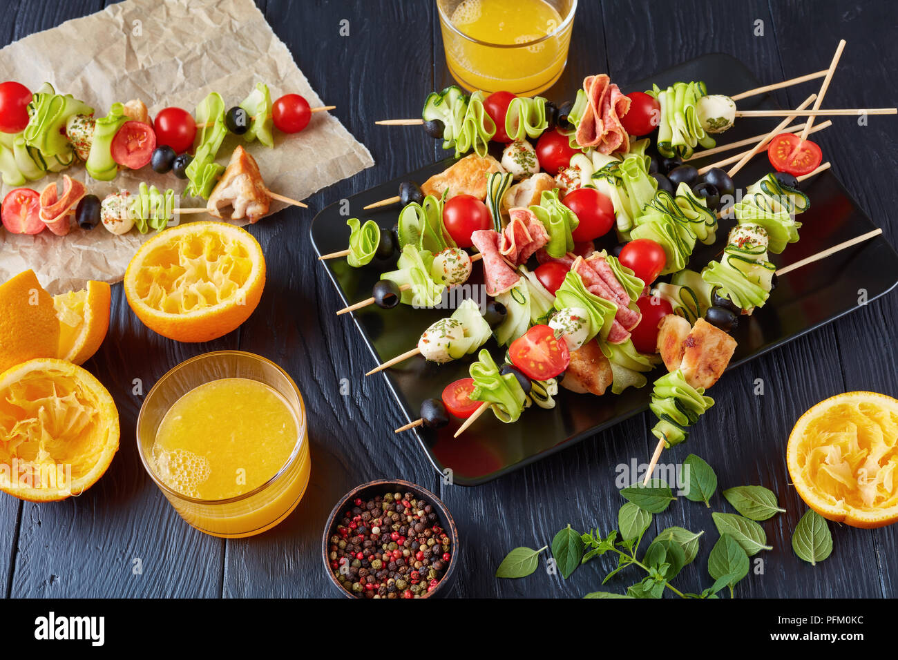 Kebab en brochettes avec la viande de poulet, courgettes, tomates, mozzarella tranches de salami, boules, des olives sur une plaque noire sur une table en bois avec du jus d'orange je Banque D'Images