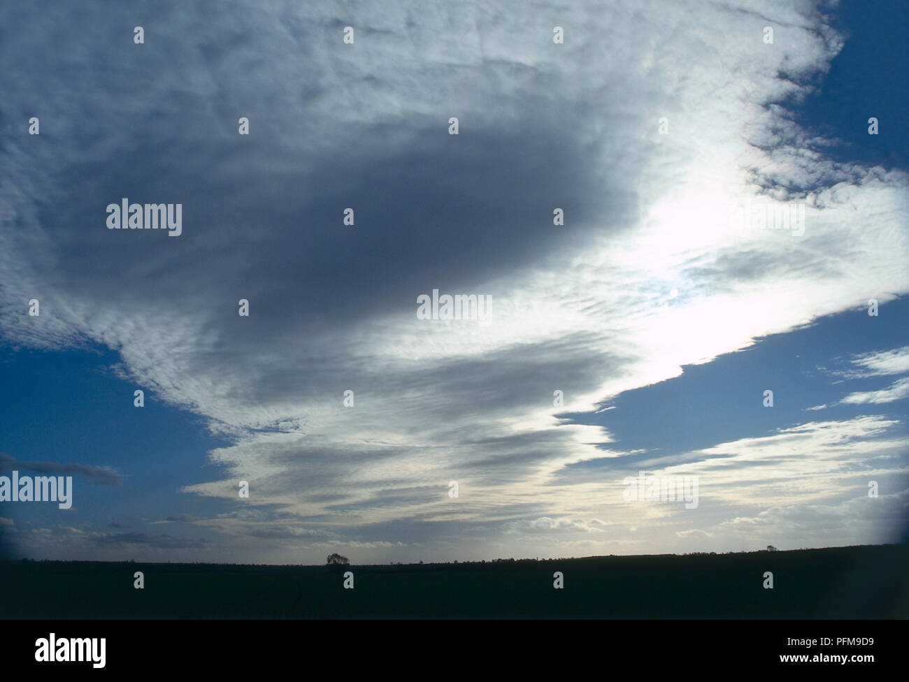 Altocumulus lenticularis, espèces, de grands nuages blancs et gris fanning à l'assombrissement du ciel bleu, du soleil illuminant les bords. Banque D'Images