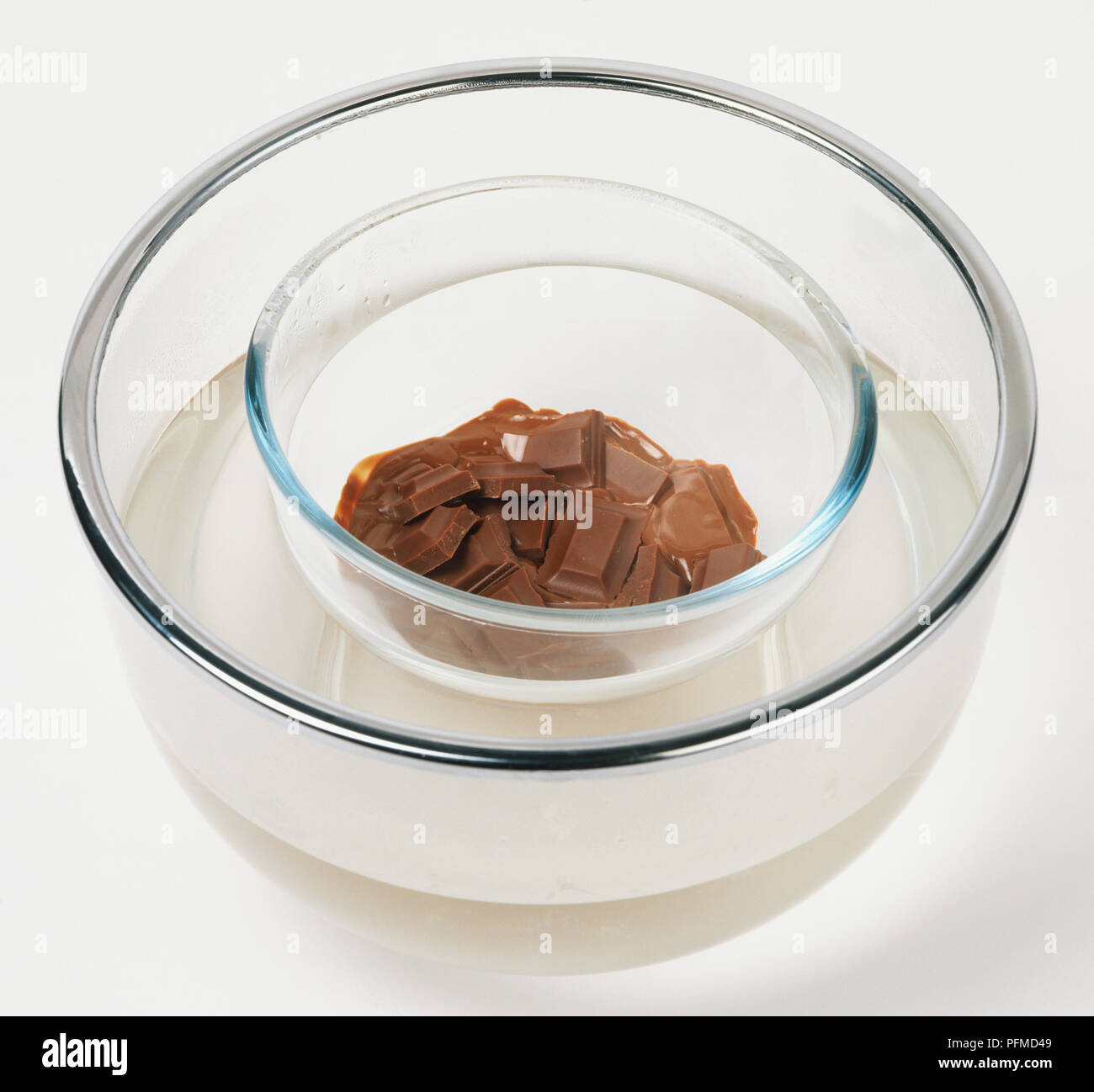 Carrés de chocolat fondant dans un bol en verre placé dans un autre bol en verre contenant de l'eau chaude. Banque D'Images