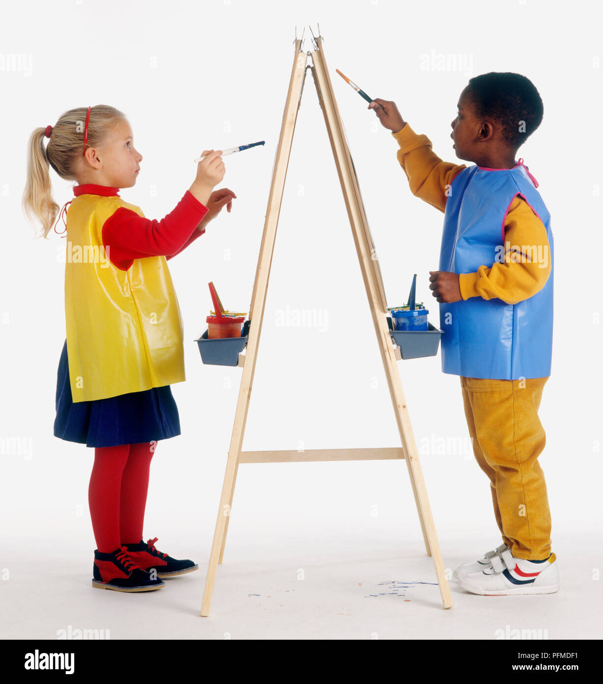 Fille et garçon portant des tabliers en plastique jaune, peinture sur bois chevalet Banque D'Images