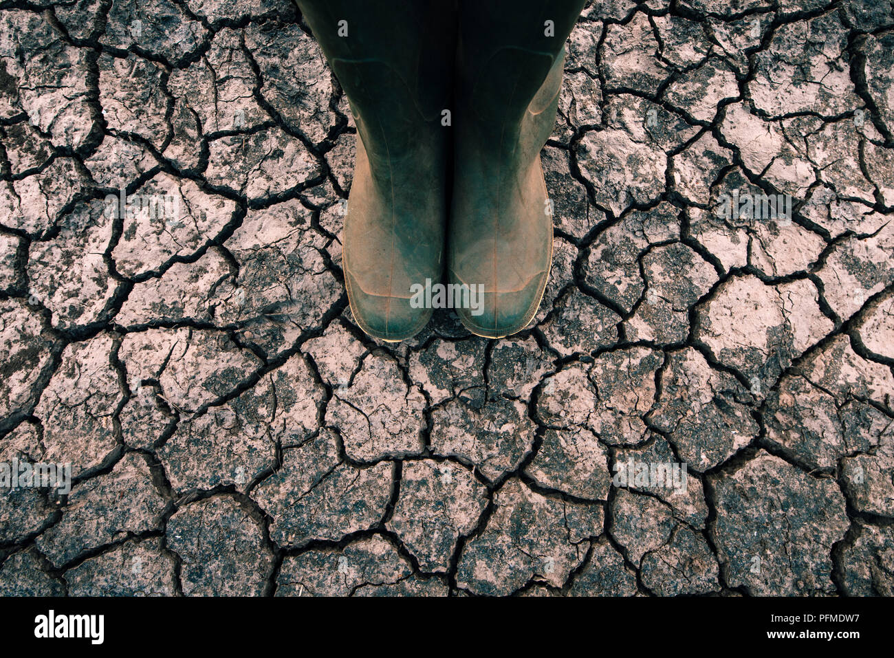 Agriculteur en bottes de caoutchouc debout sur sol sec sol, le réchauffement planétaire et le changement climatique a des répercussions sur la croissance et le rendement des cultures Banque D'Images