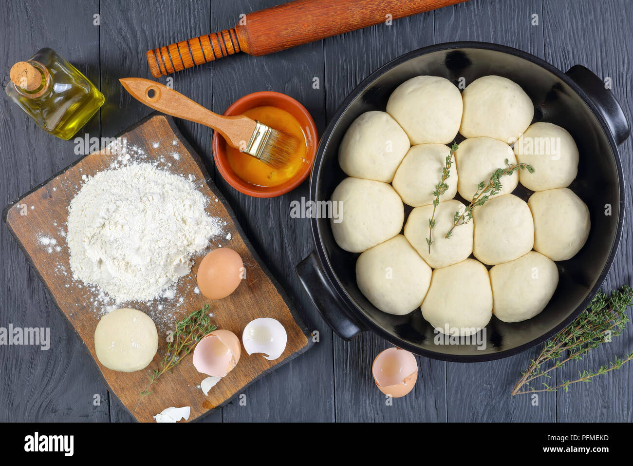 Douce et moelleuse crus de petits pains dans le plat de cuisson avec un rouleau à pâtisserie et les ingrédients sur la table de cuisine en bois, vue du dessus Banque D'Images