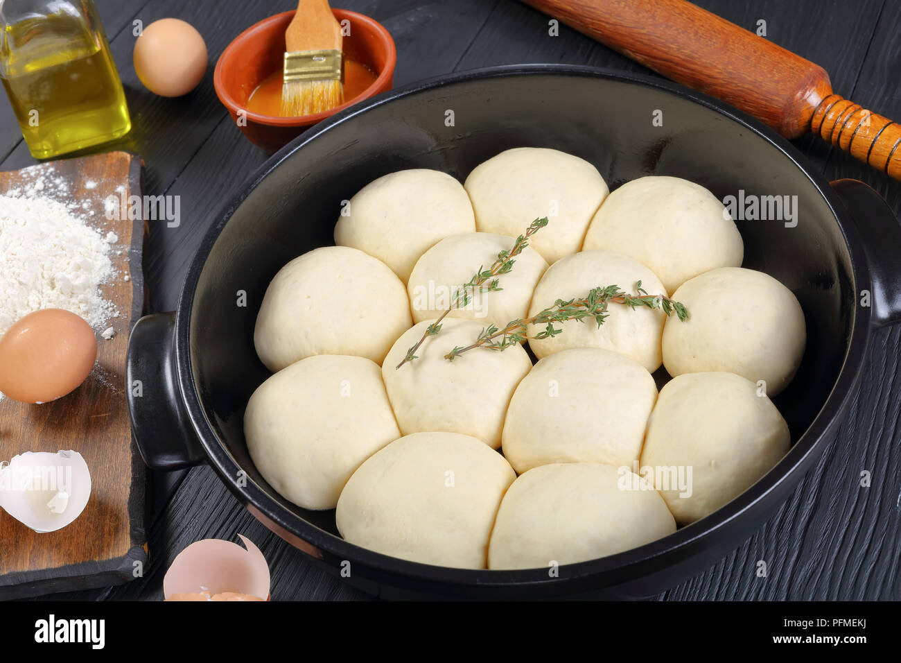 Douce et moelleuse tarte de petits pains dans le plat de cuisson avec la pâte, de la farine et des oeufs sur une planche à découper, l'huile d'olive, rouleau à pâtisserie en bois sur une table de cuisine, vue Banque D'Images