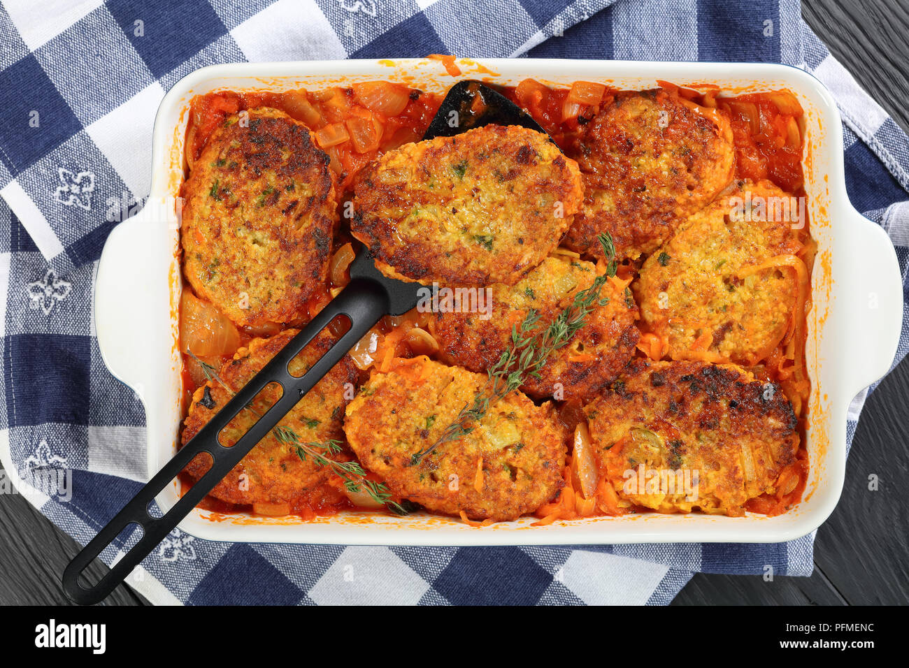 Close-up de compote de couscous cakes avec l'oignon, les carottes et la sauce tomate dans le plat de cuisson sur table en bois avec des serviettes de cuisine méditerranéenne saine , Banque D'Images