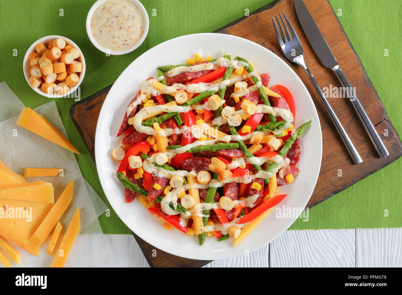 Saucisses, fromage, asperges, maïs, poivron rouge, salade de croûtons servis sur assiette blanche sur une planche à découper avec sauce maison de yogourt et ensemble de gra Banque D'Images