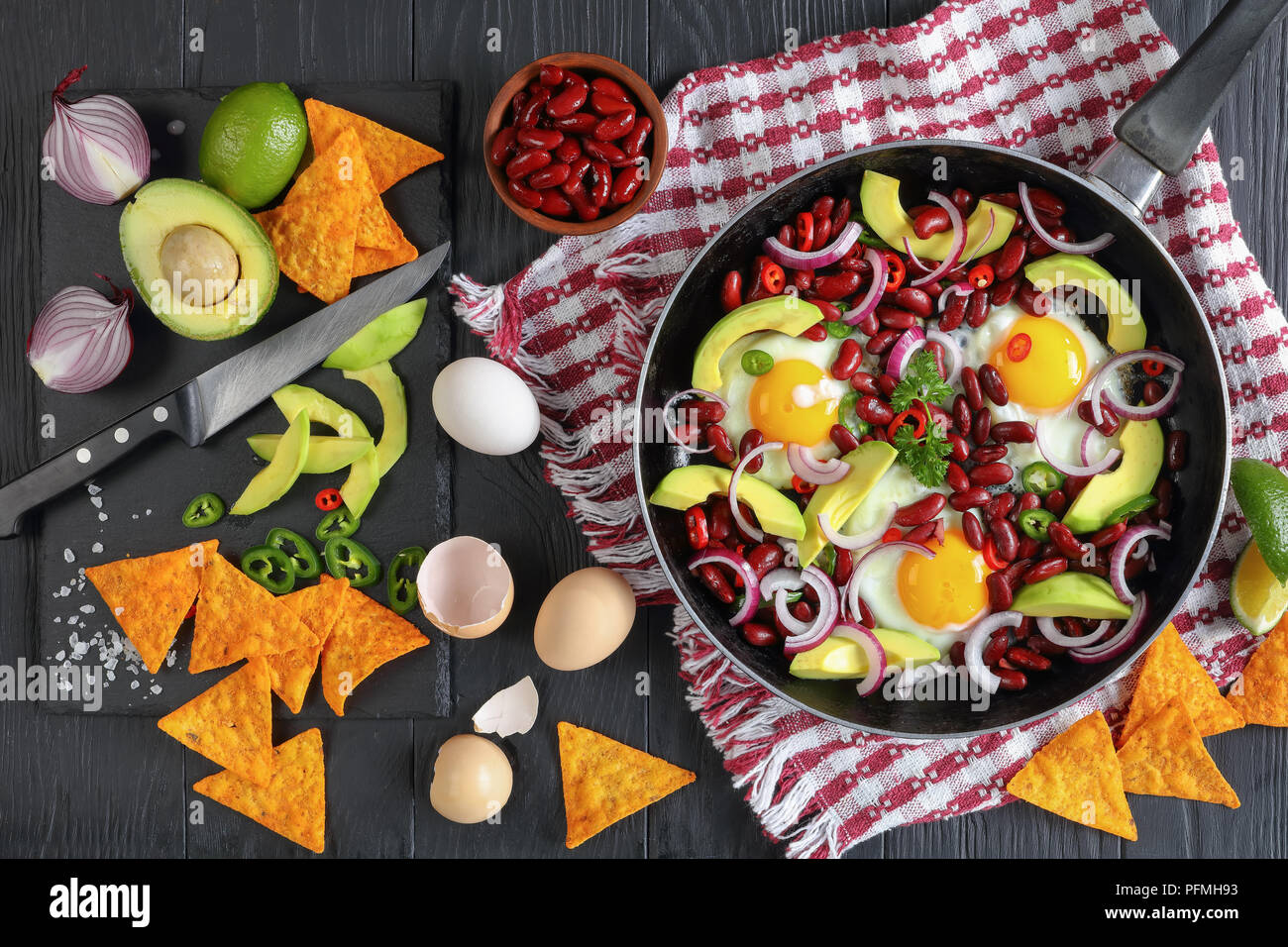 Délicieux petit déjeuner mexicain - œufs frits, haricots rouges, tranches d'avocat, d'oignon, des piments jalapeno piment fort et sur la poêle, les ingrédients et des nachos o Banque D'Images