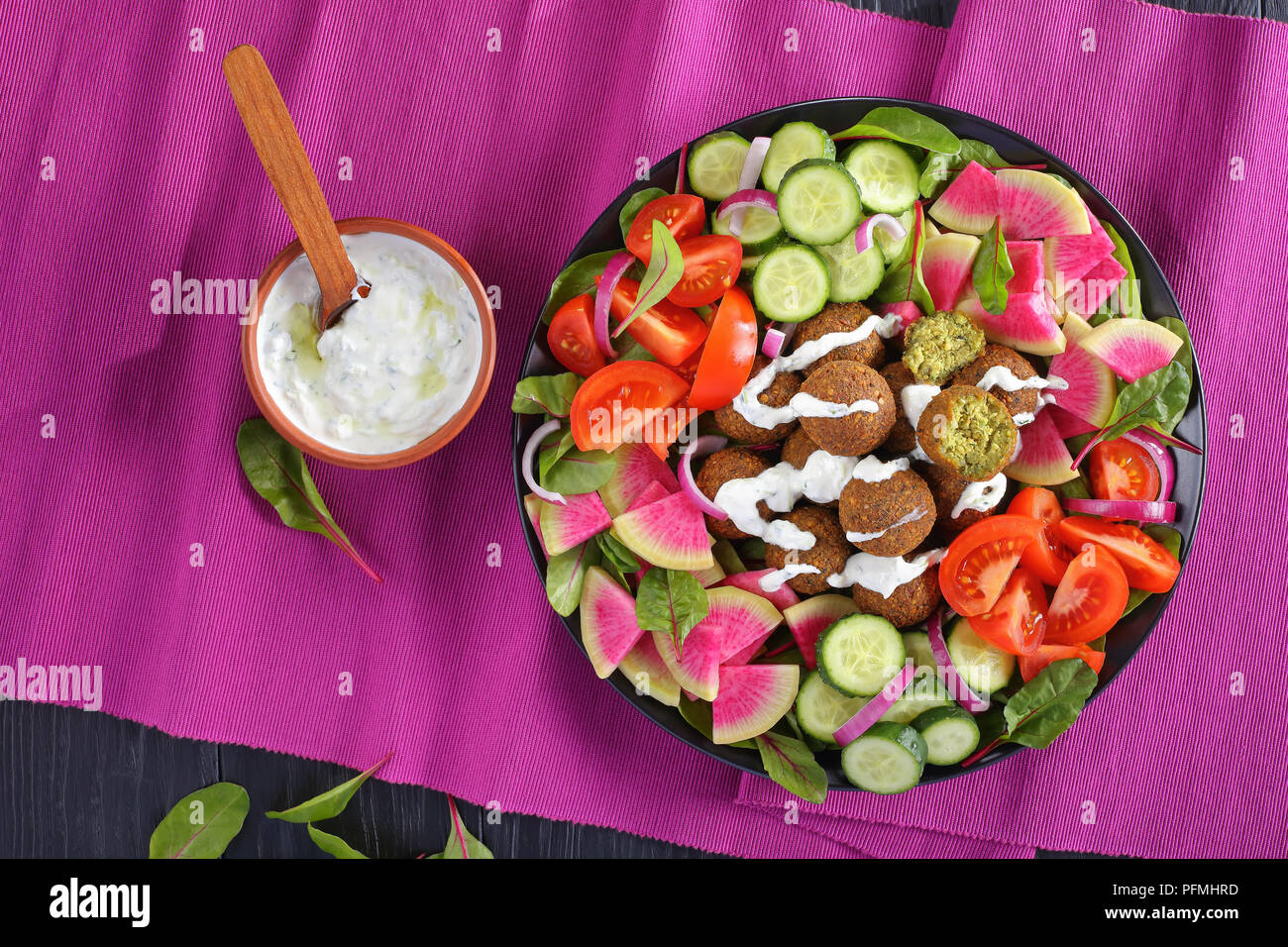 Boules de falafel frit sur la plaque avec légumes salade colorée de melon radis, concombre, feuilles de bette à carde et les tranches de tomates dans un bol de sauce tzatziki. Banque D'Images