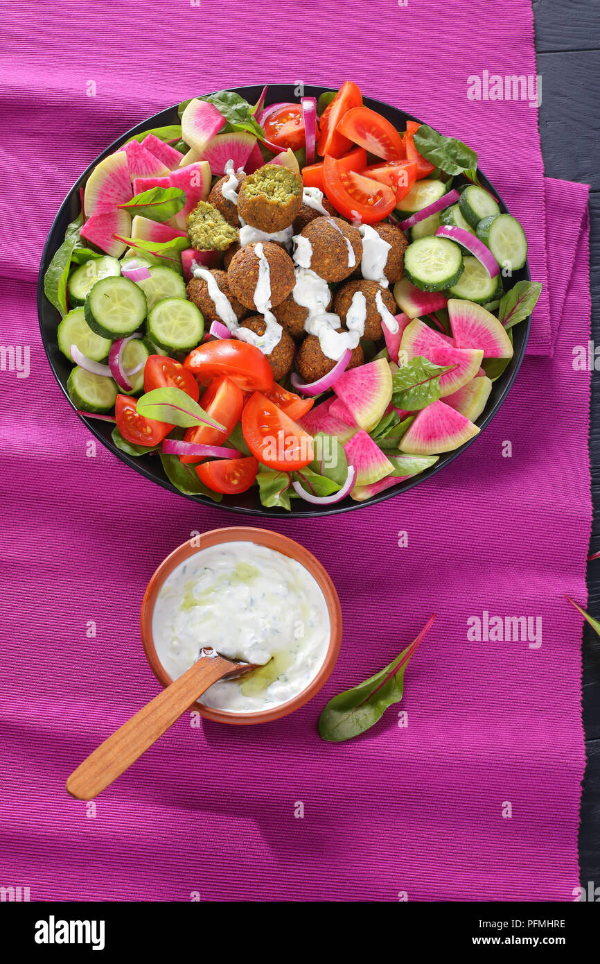 Boules de falafel délicieux sur la plaque avec légumes salade colorée de melon radis, concombre, feuilles de bette à carde et de tranches de tomate. sauce tzatziki dans bol, Banque D'Images