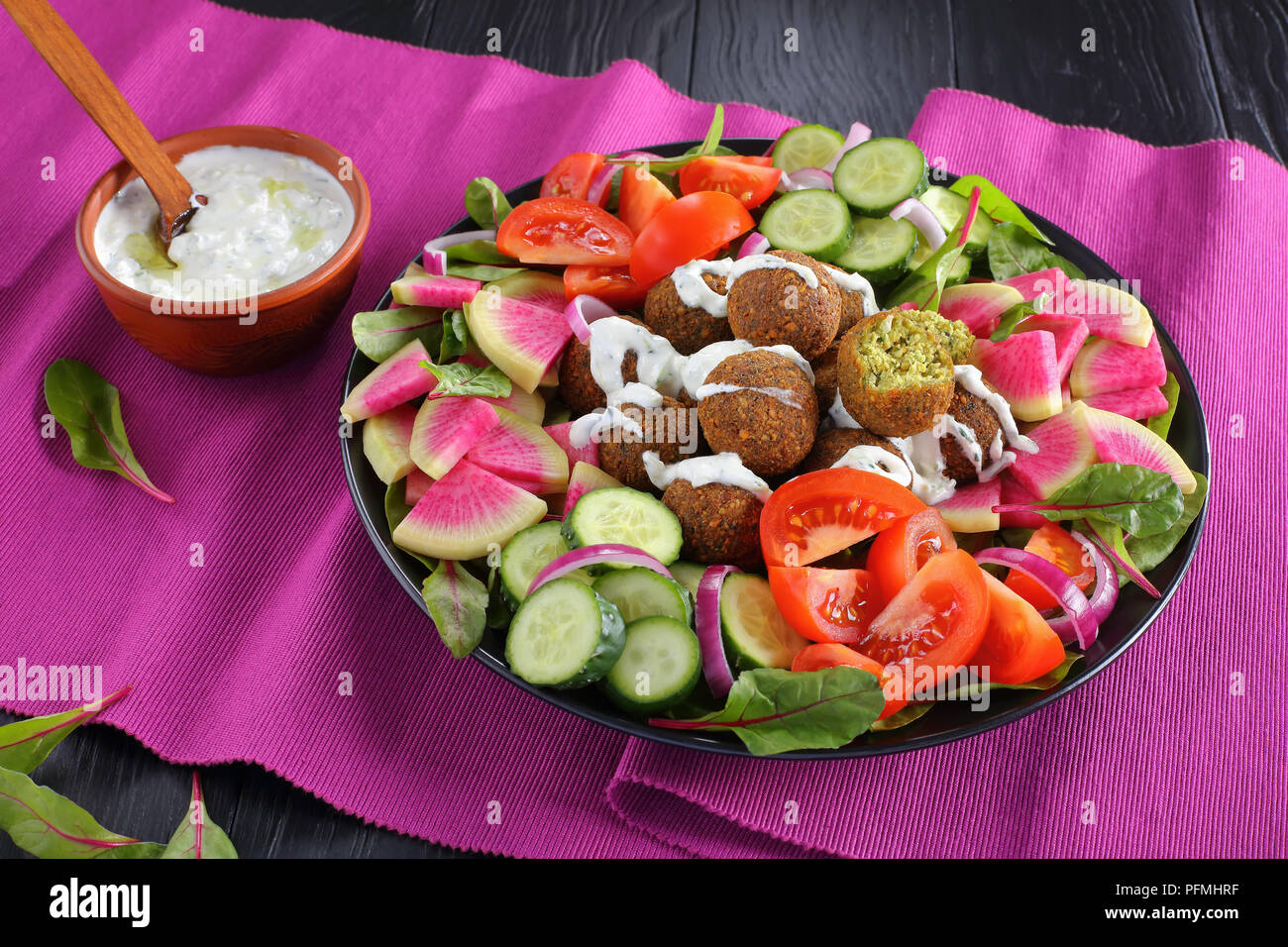 Boules de falafel savoureux sur la plaque avec légumes salade colorée de melon radis, concombre, feuilles de bette à carde et de tranches de tomate. sauce tzatziki dans bol, vie Banque D'Images