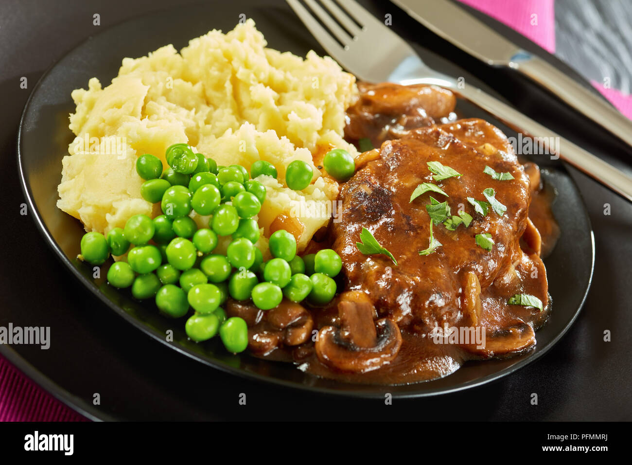 Close-up de partie de sex salé les steaks juteux salisbury avec sauce oignon champignons servi avec une purée de pommes de terre et les pois verts sur les plaques noires wit Banque D'Images