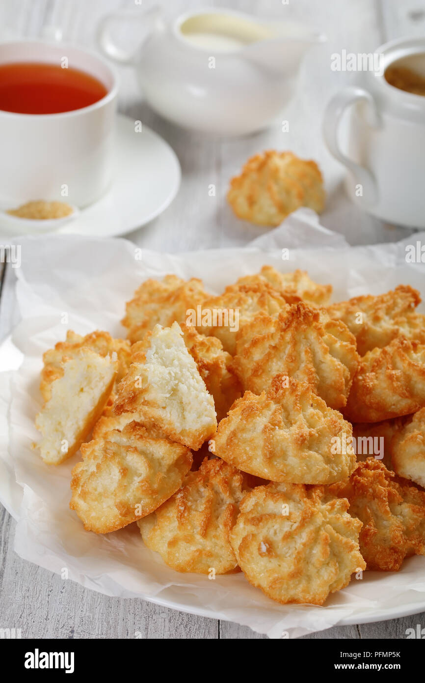 Des délicieux macarons coco cookies sur une plaque blanche sur table en bois avec tasse de thé, la cuvette et la crème fraîche dans un pot à lait à l'arrière-plan, Banque D'Images