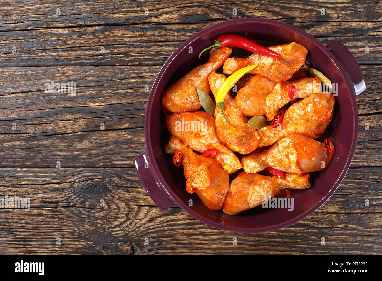 Pilons de poulet cru mariné frotté avec la spice, morceaux de piment, les feuilles de laurier prêt à cuire dans un plat, vue de dessus, l' Banque D'Images
