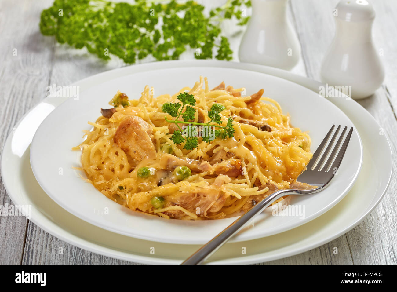 Portion de pâtes, - Tetrazzini à la crème, viande de poulet, de fromage fondu, petits pois, champignons en cocotte sur une des assiettes blanches avec un classique, la fourche d'argent Banque D'Images