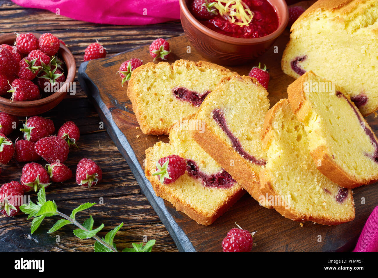 Close-up de quatre-quarts au citron avec confiture de framboises garniture sur une planche à découper une vieille table en bois avec les baies fraîches, sombre, style rustique, cuisine française Banque D'Images