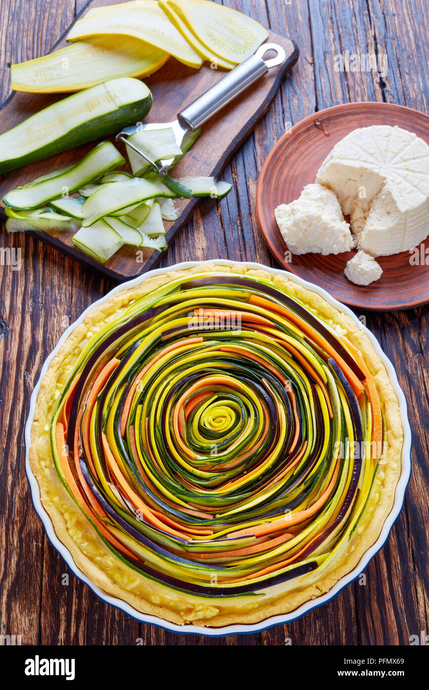 Spirale de légumes quiche à la courgette, l'aubergine, la carotte avec des tranches de fromage ricotta dans un plat allant au four, sur une vieille table rustique avec des ingrédients, v Banque D'Images