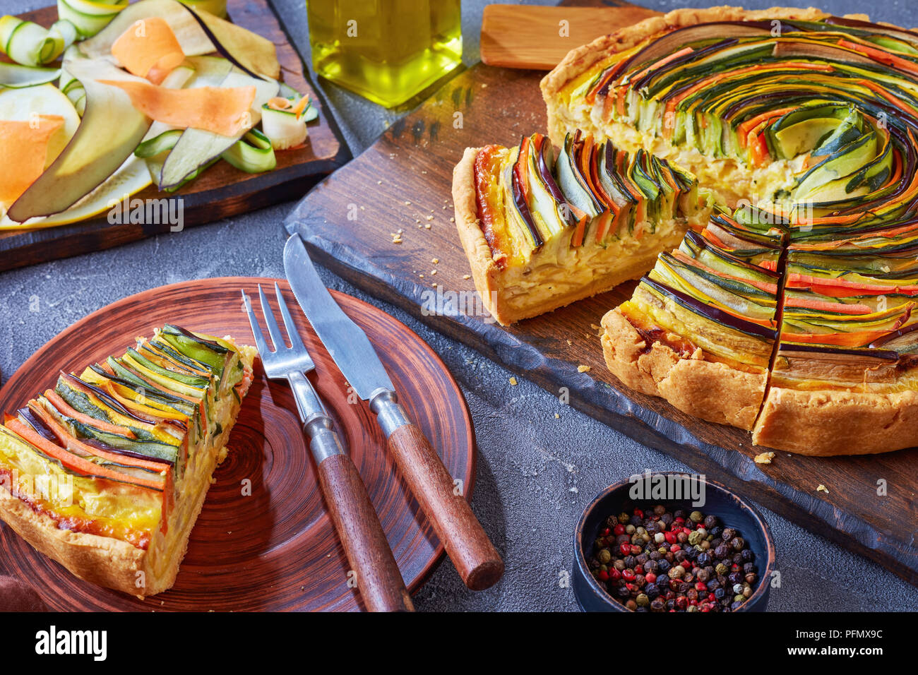 Close-up de tranches de tarte en spirale avec la courgette, l'aubergine, la carotte en lanières de fromage ricotta, servis sur une plaque d'argile avec fourchette et couteau, voir à partir de Banque D'Images