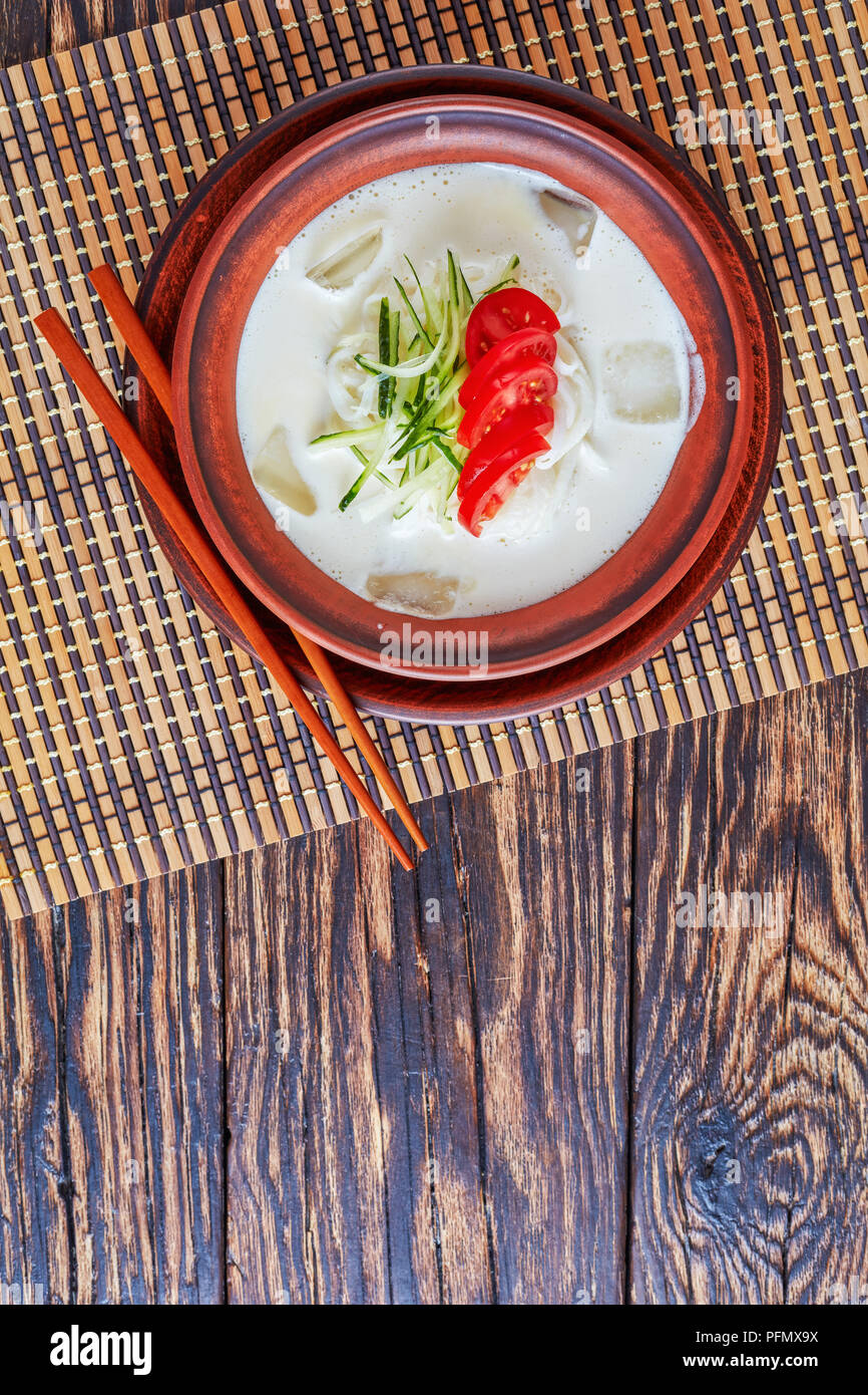 Kongguksu, kong-guksu - délicieux d'été froide soupe coréenne avec du lait de soja et nouilles de riz garnie de lanières de concombre et de tranches de tomate, vue horizontale Banque D'Images