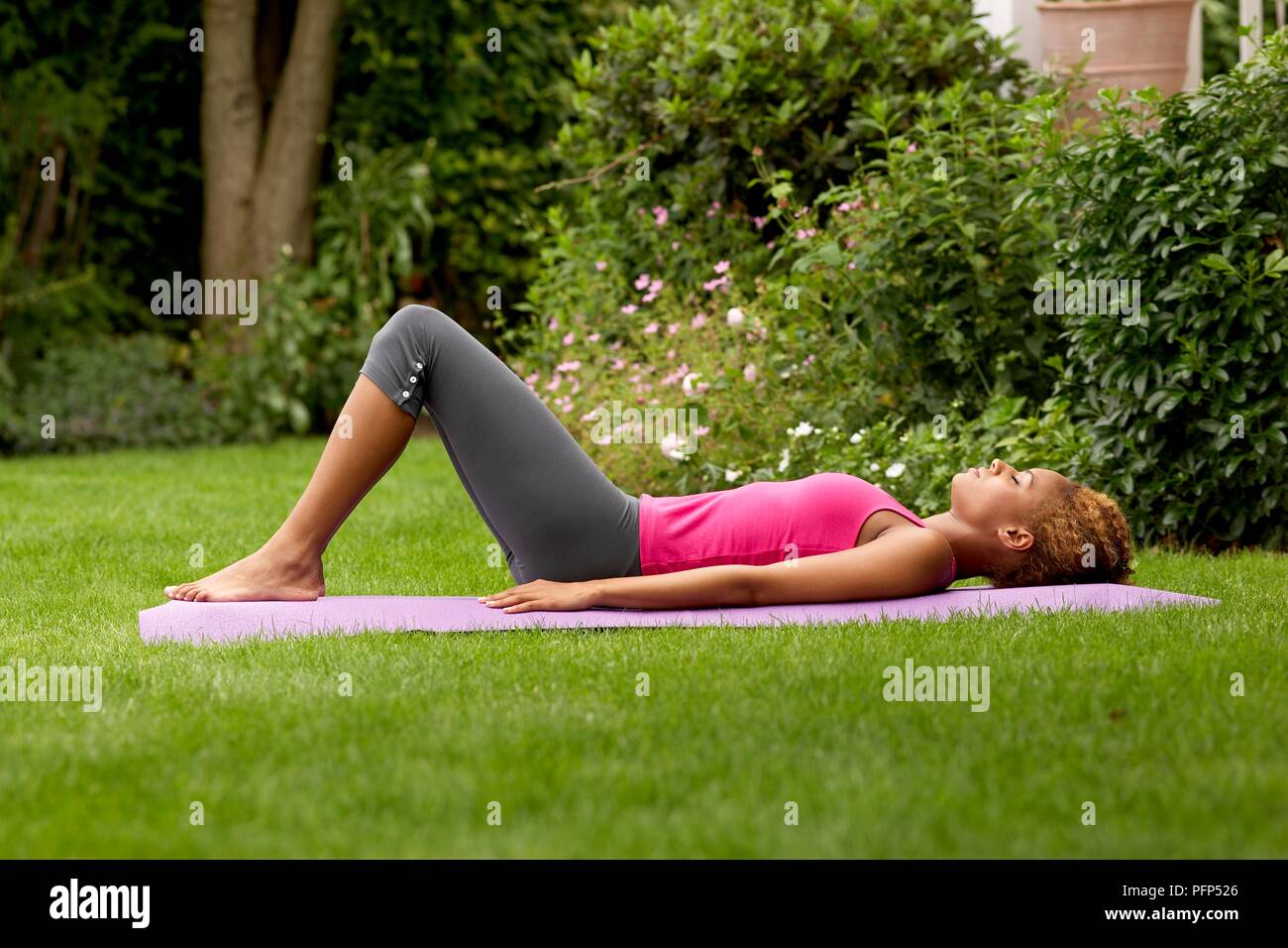 Jeune femme en leggings et haut rose allongée sur le dos au jardin avec ses jambes pliées, side view Banque D'Images