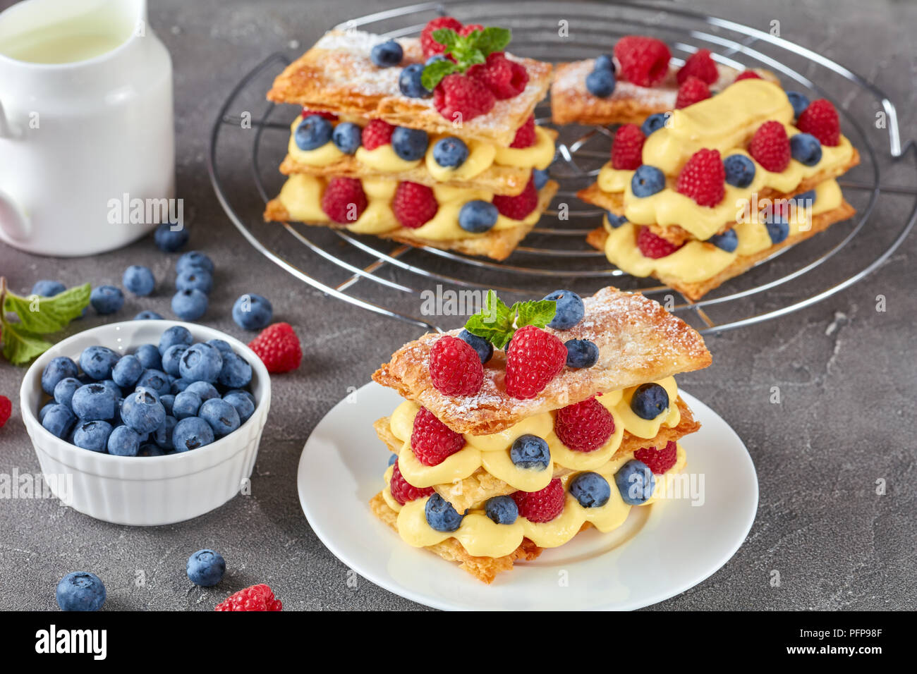 Le français dessert millefeuille de pâte feuilletée et crème pâtissière, framboises, bleuets sur une plaque avec de la crème fraîche et des petits fruits sur une table, vue d'un Banque D'Images