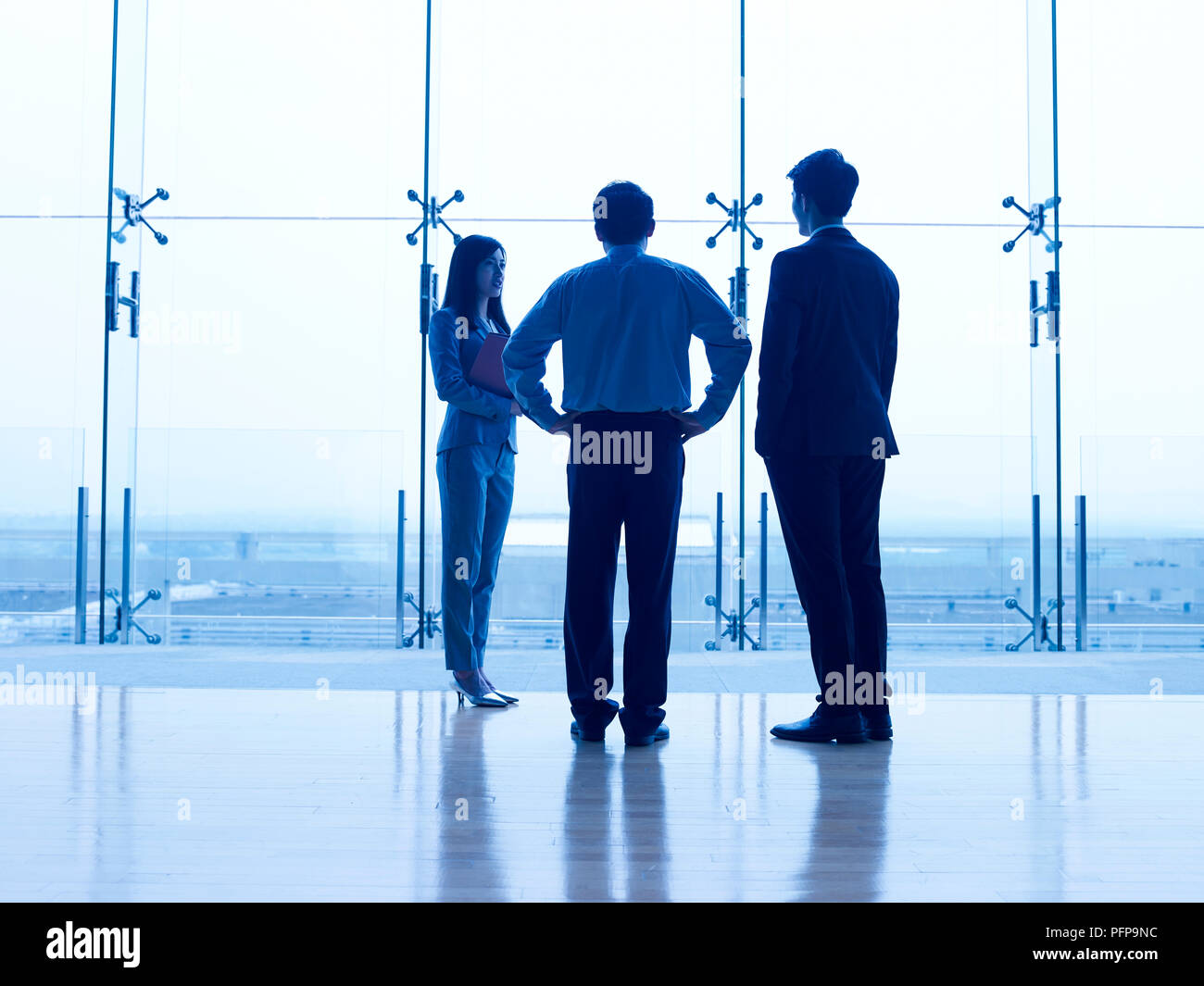 Silhouettes de trois dirigeants de sociétés asiatiques debout devant la fenêtre de discuter affaires. Banque D'Images