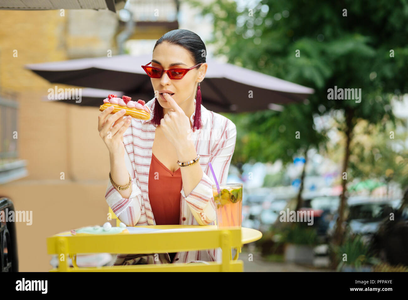 Jolie femme en rouge lunettes de lécher son doigt tout en mangeant son dessert Banque D'Images