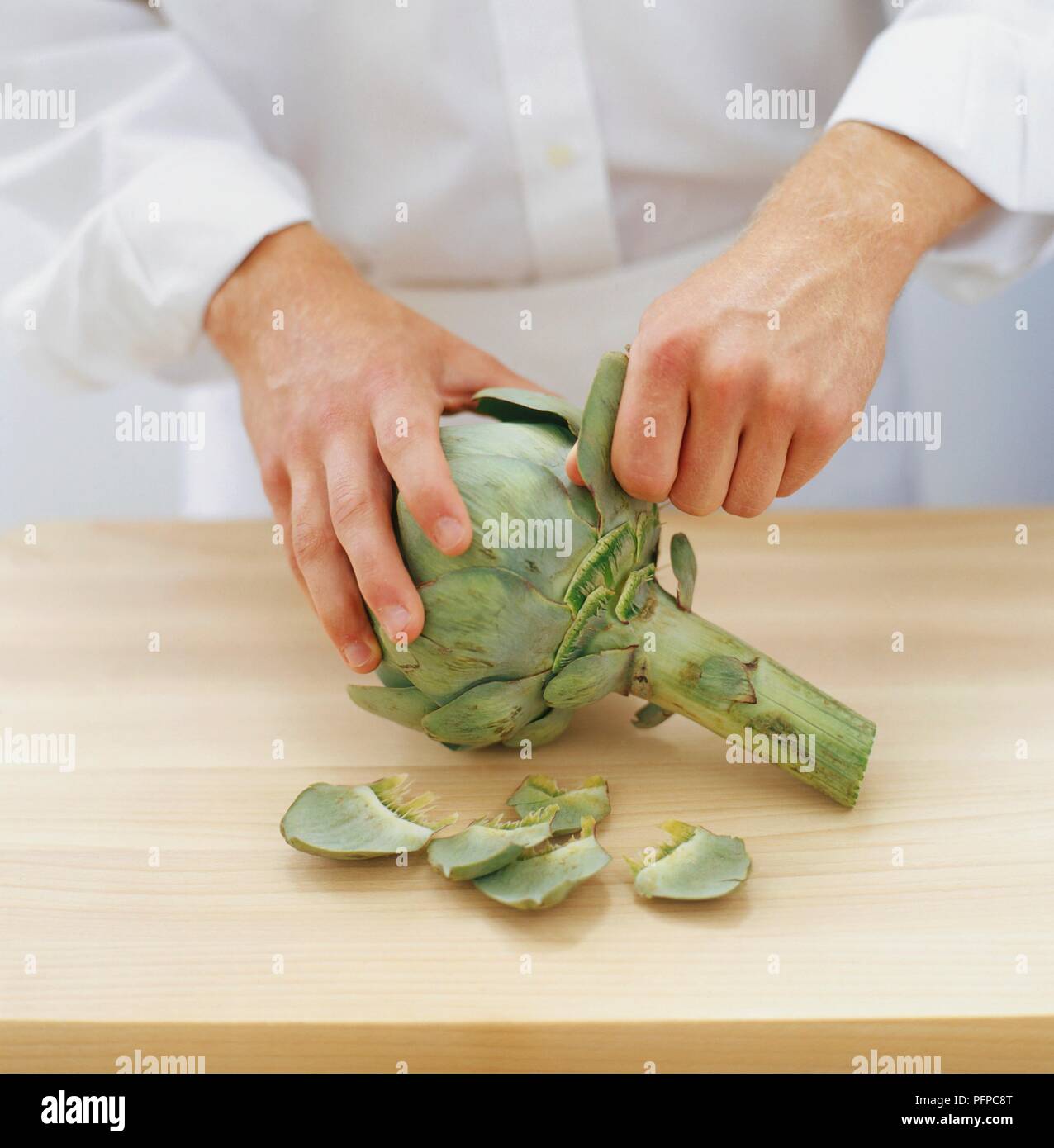 Chef en utilisant les mains pour retirer les feuilles extérieures de l'artichaut Banque D'Images
