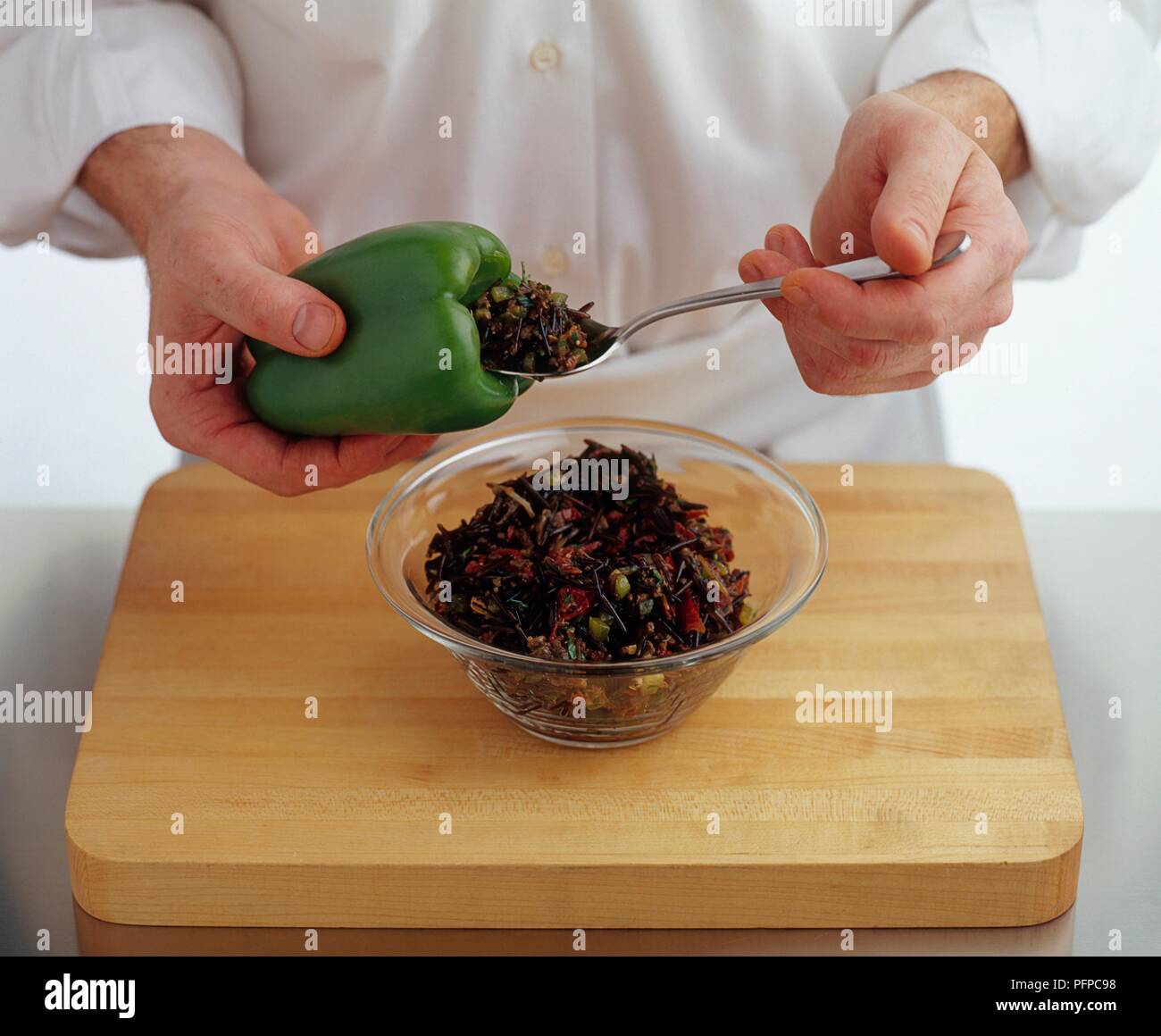 Chef cuisinier avec cuillère pour mettre le riz sauvage de farce à l'intérieur du poivre vert Banque D'Images