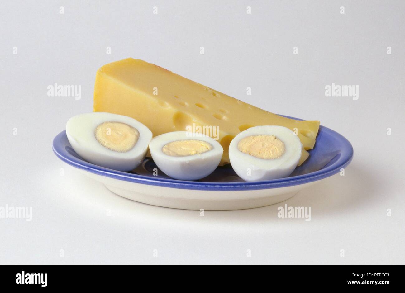 Tranche de fromage Edam et de trois moitiés d'oeufs durs sur plaque bleue Banque D'Images